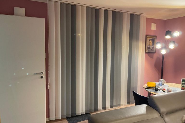 Jalousien in Köln Ein Wohnzimmer mit vertikalen Jalousien, einer Lampe und einem Tisch.
